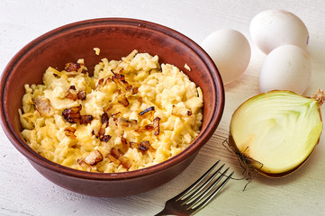 Traditional small paste from Liechtenstein. Dish with egg and fried onions. Rustic food in an old clay plate. A simple dinner and a fork on a white wooden table.