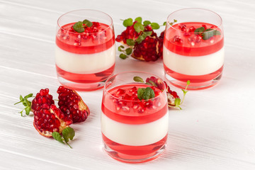 Creamy vanilla panna cotta with red jelly in beautiful glasses, fresh ripe pomegranate on white...