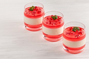 Creamy vanilla panna cotta with red jelly in beautiful glasses, fresh ripe pomegranate on white...