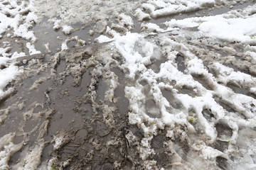 Dirty road with foot prints on wet soil and melting snow