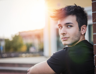 Friendly attractive young man looking at camera, large copy-space next to him, in urban environment