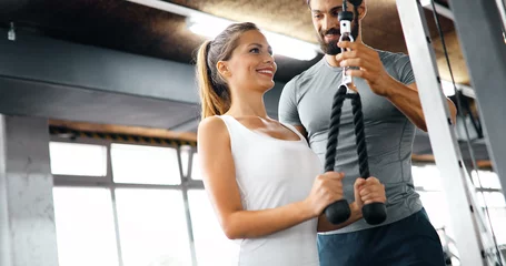 Tuinposter Young beautiful woman doing exercises with personal trainer © NDABCREATIVITY