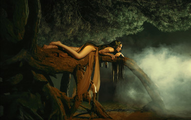 A fabulous, forest nymph with long hair lies on a tree branch with an aggressive look. Background...