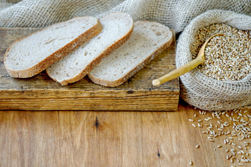 On a wooden board lie slices of bread. Nearby is a sack of wheat.