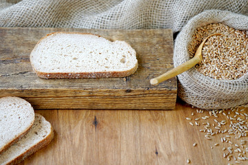 On a wooden board lie slices of bread. Nearby is a sack of wheat.