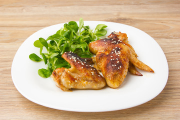 Fried chicken wings. Chicken wings of a barbecue on a white plate with salad. Cornsalad on a plate with wings.