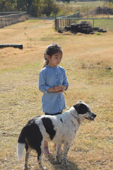 little girl wearing denim outfits touching black and white dog in a farm, filtered tones
