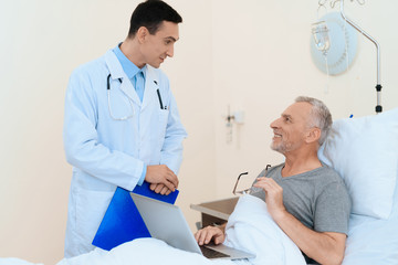 Obraz premium An elderly man lies in a hospital room on a bed. He is undergoing rehabilitation. A doctor came to see him.