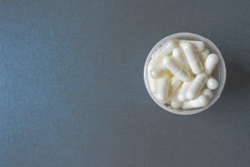 Close up of white pills or capsules in container or bottle on colorful background, medication or...