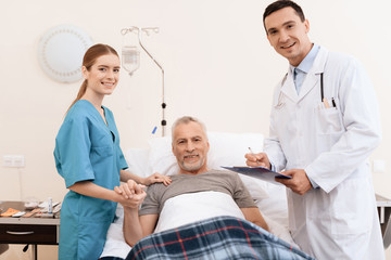 Obraz premium The old man lies on a cot in the medical ward, and next to him there is a doctor and a nurse.