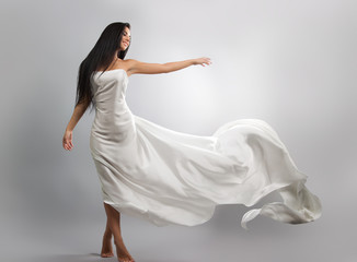 fashion photo of young girl in white dress flying tissue. Lightweight material. Grey background