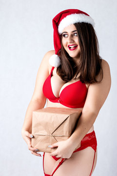 Happy fat Santa girl. Model in red lingerie and Santa hats. XXL a woman celebrating Christmas and a new year. Holds a great gift