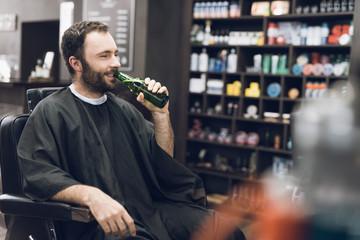 A man drinks alcohol in the hairdresser's armchair of a modern barbershop.