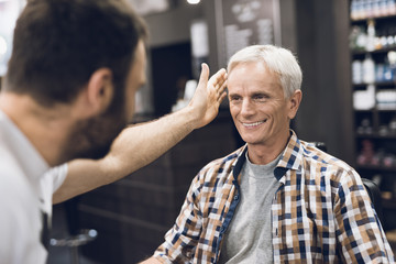 The old man is sitting in the barber's chair in a man's barbershop, where he came to cut his hair.