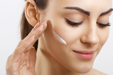 Happy young woman applying cream to her face. Skincare and cosmetics concept.Cosmetics. Woman face...