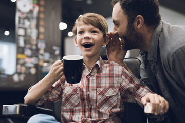 The boy listens to an adult man sitting in a barbershop hairdresser's chair.