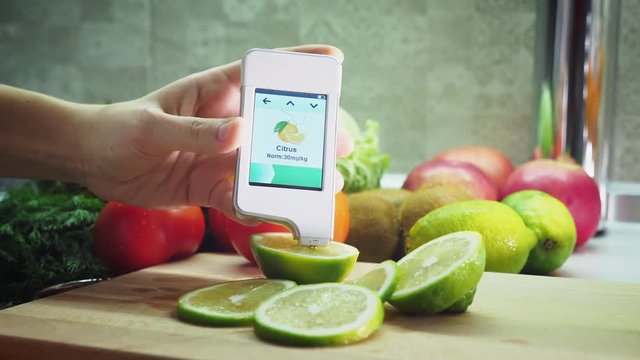 Measurement of the amount of nitrates in the green lemon by a portable digital device in the kitchen. On the device screen shows the low nitrate content