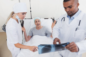 A nurse and a doctor are standing next to a patient with cancer. The doctor is holding her X-ray.