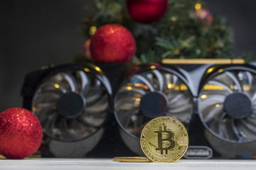 биткоин монета лежит на видеокарте под рождественской елкой с шарами 