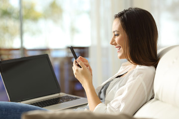 Woman using a phone and a laptop at home