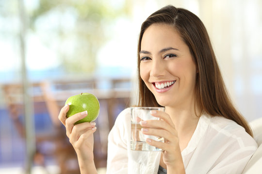 Happy woman holding an apple and a glass of water