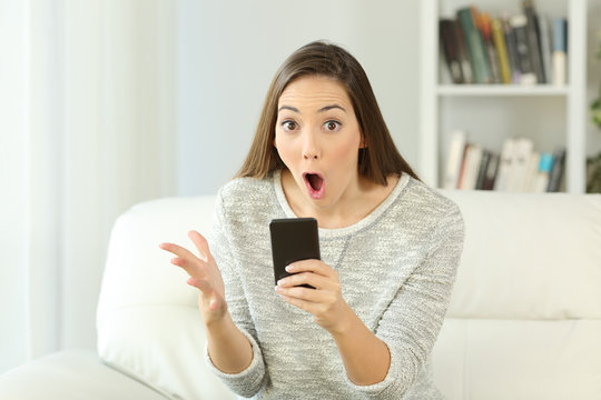 Surprised woman holding a phone looking at you