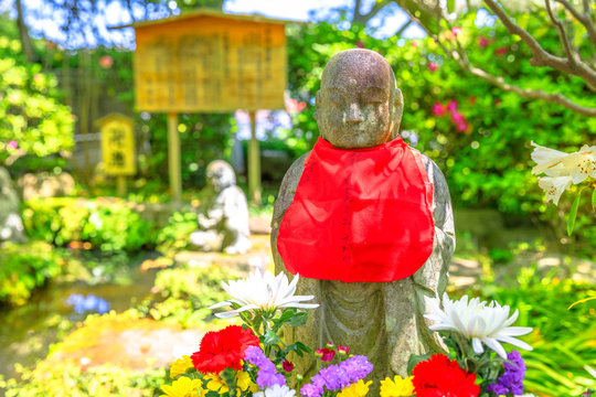 Close up of stone Jizo statue with red scarf on his neck on blurred background. Hase-dera in Kamakura, Japan. Hasedera is one of the largest Buddhist temples in the city. Japanese culture concept