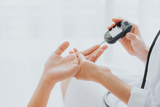 Doctor use glucosmeter checking blood sugar level from patient hand