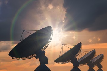 Silhouettes of array of satellite dishes or radio antennas at sunset. - obrazy, fototapety, plakaty
