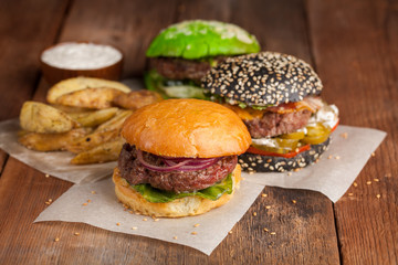 Set of three mini homemade Burger, Idaho potatoes with sauce and vegetables on a old wooden background. the concept of junk food and fast food