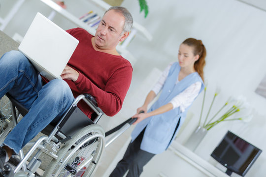 disabled man watching movie on laptop while cleaner is working