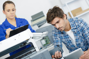 young male technician using a tablet for repairing photocopier