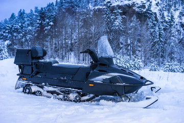 Black snowmobile on a background of snow-covered rock.