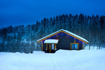 Wooden house on a background of snow-covered forest. Camping in the forest. Cottage in winter.