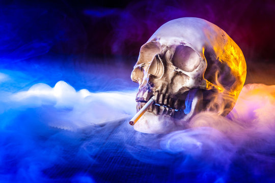 The skull of a man in tobacco smoke. The skull smokes a cigarette.