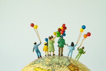 miniature people figure back view of happy family holding balloons standing on globe as looking...