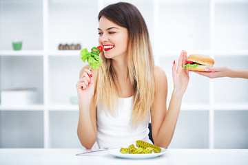 Dieting concept, beautiful young woman choosing between healthy food and junk food