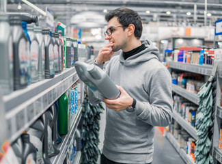 male customer buying engine lubricating oil in the car supermarket. Difficult decision which motor...