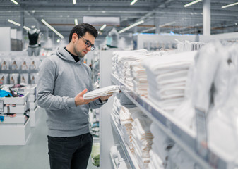 Male Customer inspecting and buying towels in supermarket. White clean towels