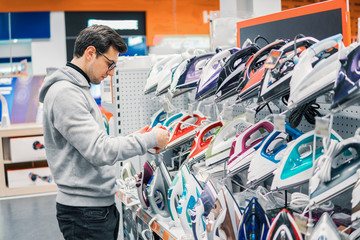 Smart customer buying clothes iron in hypermarket. difficult decision. Various choice. Shopping concept. He is holding device and examining it.