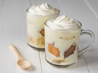 Banana pudding with cookies and whipped cream on a wooden table with a small wooden spoon.