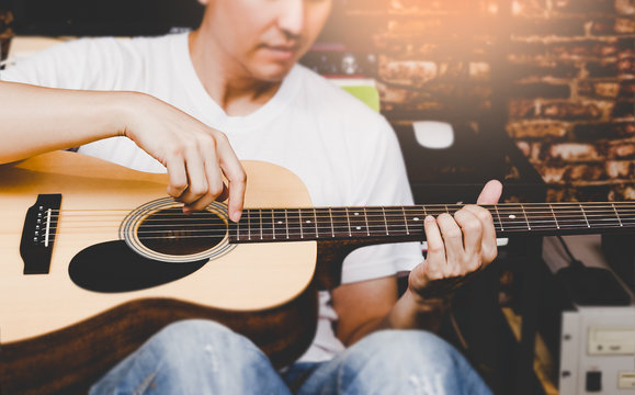 asian man playing acoustic guitar, focus on hands