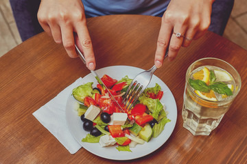 Hands with fork and knife. Salad and drink on table