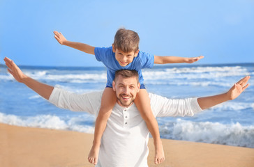 Cute little boy with father on sea beach at resort