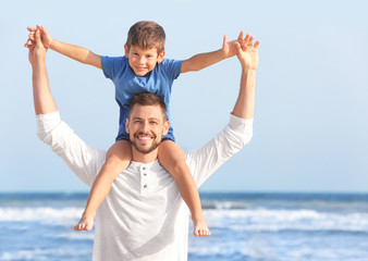 Cute little boy with father on sea beach at resort