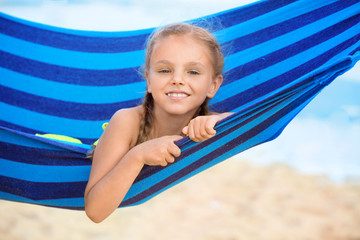 Cute little girl lying in hammock on sea beach at resort