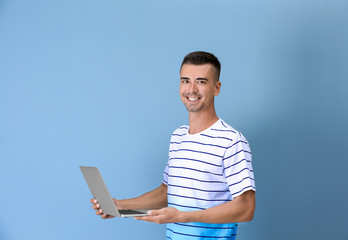 Young man with laptop on color background