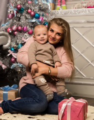 Fototapeta na wymiar Happy mother with newborn son, sitting on a floor near a Christmas tree. Waiting for a holiday.