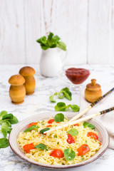 Noodles with pepper, lettuce leaves and sesame seeds in a ceramic plate and chopsticks