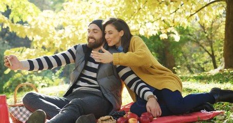 Young attractive couple having video chat on the smart phone in the yellow park on sunny autumn day. Outdoor